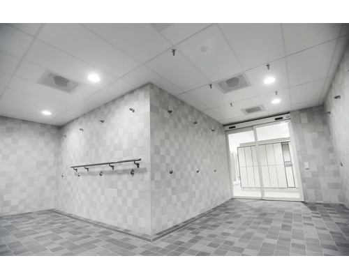 Espace de douche commune moderne et spacieux avec carrelage mural et de sol clair et une porte coulissante en verre menant au vestiaire.