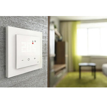 Thermostat mural intelligent avec affichage numérique de la température et connexion wifi et touches tactiles dans un salon lumineux.