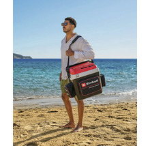Un homme porte un sac isotherme Einhell avec bandoulière et poches latérales sur une plage de sable lumineuse au bord de la mer. Einhell Logo.