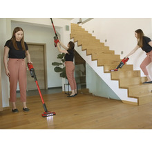 Une femme utilise un aspirateur balai rouge pour les sols, murs et escaliers en bois dans une pièce moderne et lumineuse.