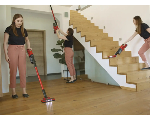 Une femme utilise un aspirateur balai rouge pour les sols, murs et escaliers en bois dans une pièce moderne et lumineuse.