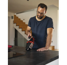 Un homme nettoie des grains de café sur un plan de travail de cuisine à l aide d un aspirateur à main Einhell dans un intérieur moderne.