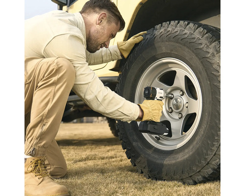 Un homme utilise une boulonneuse à chocs sans fil pour desserrer les écrous de roue sur un pneu de véhicule tout-terrain à l'extérieur.