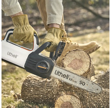 Une personne portant des gants de travail coupe un épais tronc d'arbre à l'extérieur avec une tronçonneuse à batterie Litheli.