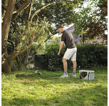 Homme effectuant l'entretien du jardin avec un coupe-bordure électrique et une station électrique portable sur une pelouse sous des arbres.