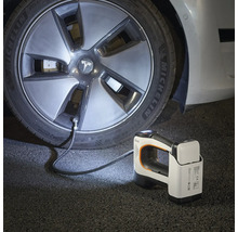 Compresseur portable à batterie gonflant un pneu de voiture dans l'obscurité, avec lampe intégrée et batterie amovible.