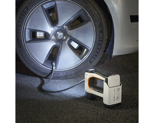 Compresseur portable à batterie gonflant un pneu de voiture dans l'obscurité, avec lampe intégrée et batterie amovible.