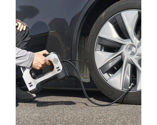 Une personne utilise un compresseur d'air électrique portable pour gonfler un pneu de voiture.
