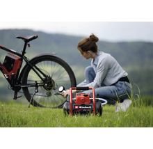 Une femme gonfle le pneu arrière d'un vélo avec un compresseur à batterie Einhell en extérieur sur l'herbe.