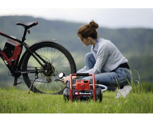 Une femme gonfle le pneu arrière d'un vélo avec un compresseur à batterie Einhell en extérieur sur l'herbe.