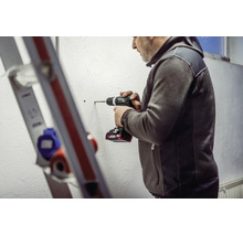 Mann bohrt mit einem Metabo Akku-Bohrschrauber ein Loch in eine Wand. Im Vordergrund ist eine Leiter zu sehen.