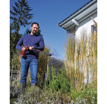 Un homme utilise un nettoyeur haute pression sans fil dans un jardin avec des herbes ornementales.