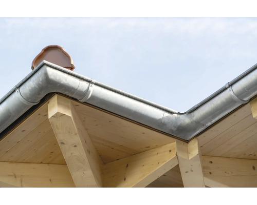 Gouttière en zinc montée sur une structure de toit en bois avec des tuiles visibles.