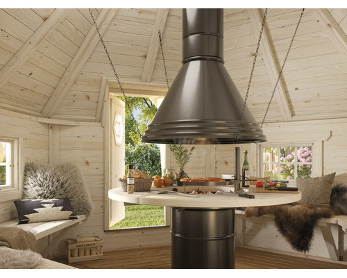 Innenansicht einer hellen Grillkote aus Holz mit zentralem runden Grilltisch, einer großen Abzugshaube aus Metall und Sitzbänken mit Kissen.
