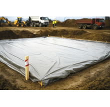 Grande bâche de protection grise étalée sur le sol d'un chantier avec des camions de chantier en arrière-plan.