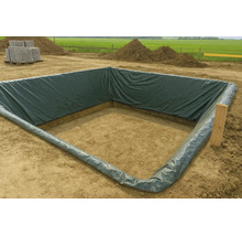 Une fosse de construction carrée tapissée d'un film PE vert foncé sur un chantier avec des tas de terre à l'arrière-plan.