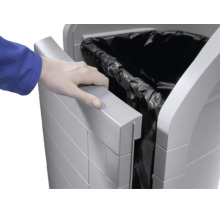 Une main ouvre une poubelle en plastique grise avec un sac poubelle noir inséré.