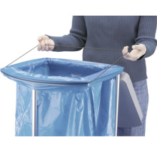 Une personne fixe un sac poubelle bleu avec un cordon sur un collecteur de déchets en métal.