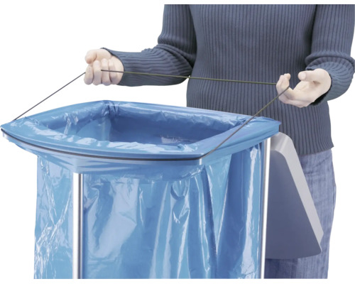 Une personne fixe un sac poubelle bleu avec un cordon sur un collecteur de déchets en métal.
