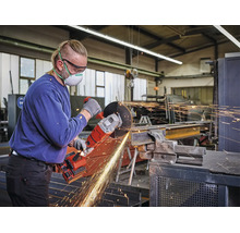 Ein Handwerker in einer Werkstatt nutzt einen Akku-Winkelschleifer zum Trennen eines Metallträgers. Er trägt Schutzbrille, Atemschutz und Handschuhe.