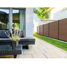 Terrasse moderne avec meubles de jardin en rotin foncé, pavés gris clair et clôture de protection brune à côté d'une pelouse.