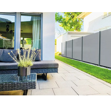 Brise-vue moderne de panneaux gris clair avec poteaux foncés dans un jardin à côté d'une terrasse avec meubles de salon et pelouse.