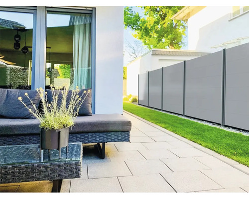 Brise-vue moderne de panneaux gris clair avec poteaux foncés dans un jardin à côté d'une terrasse avec meubles de salon et pelouse.
