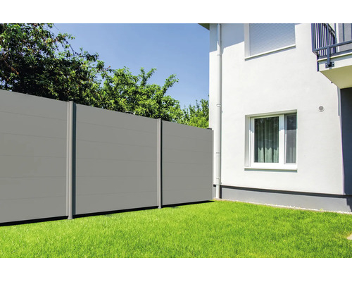Clôture brise-vue grise composée de panneaux horizontaux dans un jardin à côté d'une maison blanche sur une pelouse.