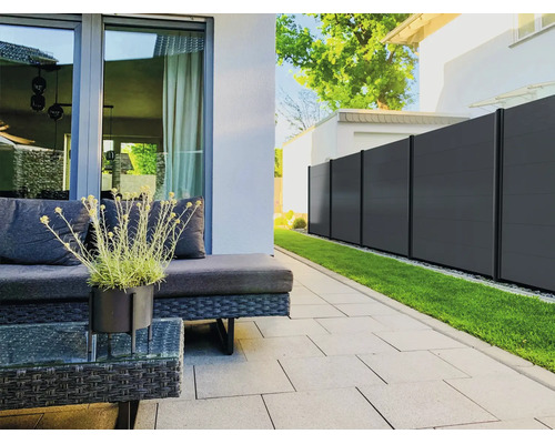 Clôture brise-vue moderne en anthracite sur une terrasse organisée avec dalles grises, meubles de jardin en résine tressée et pelouse.