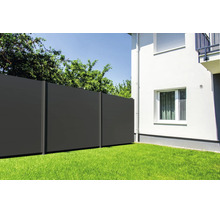Clôture brise-vue moderne composée de panneaux foncés dans un jardin sur une pelouse à côté d'une maison.