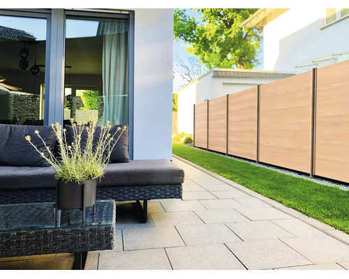 Terrasse moderne avec des dalles gris clair, meubles de jardin en polyrotin foncé et clôture brise-vue aspect bois.