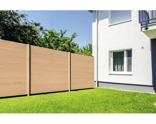 Clôture brise-vue moderne en bois composite installée sur une pelouse à côté d'un mur de maison blanc avec fenêtre.