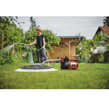 Einhell Gartenpumpe auf Rasen, verbunden mit Wasserquelle und Schlauch zur Bewässerung von Pflanzen in einem hellen, organisierten Garten.