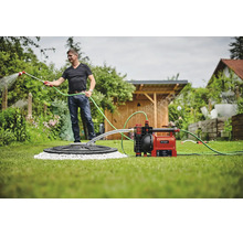 Un homme arrosant le jardin avec une pompe de jardin automatique Einhell raccordée à une citerne.
