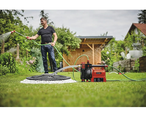 Un homme arrosant le jardin avec une pompe de jardin automatique Einhell raccordée à une citerne.