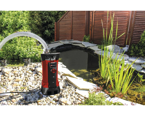 Pompe pour eaux chargées Einhell avec tuyau à côté d'un bassin de jardin avec pierres et plantes.