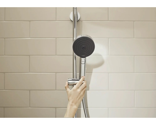 Hansgrohe Handbrause an einer Duschstange montiert, bedient von einer Hand vor einer gefliesten Wand.