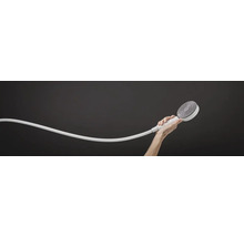 Une main tient une douchette ronde avec flexible de douche devant un fond neutre