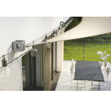Fixation murale pour voile d'ombrage avec câble en acier tendu et guirlande lumineuse sur une terrasse.