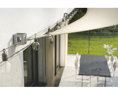 Fixation murale pour voile d'ombrage avec câble en acier tendu et guirlande lumineuse sur une terrasse.