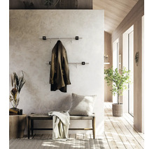 Vestiaire mural moderne avec deux barres en acier inoxydable dans un couloir lumineux avec des éléments en bois, un banc et une plante.