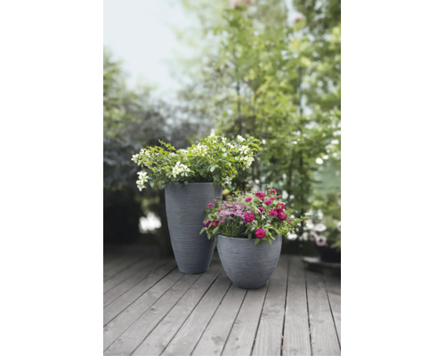 Deux bacs à fleurs gris avec structure rainurée, plantés de fleurs sur une terrasse en bois dans le jardin.