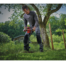 Ein Handwerker nutzt einen akkubetriebenen Erdbohrer im Garten für Erdarbeiten in der Wiese.