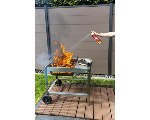 Une personne éteint les flammes d un barbecue au charbon de bois avec une bombe extinctrice dans un jardin devant une clôture.