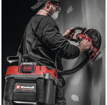 Artisan utilisant une ponceuse murale sans fil Einhell avec aspirateur sans fil raccordé pour poncer un mur.