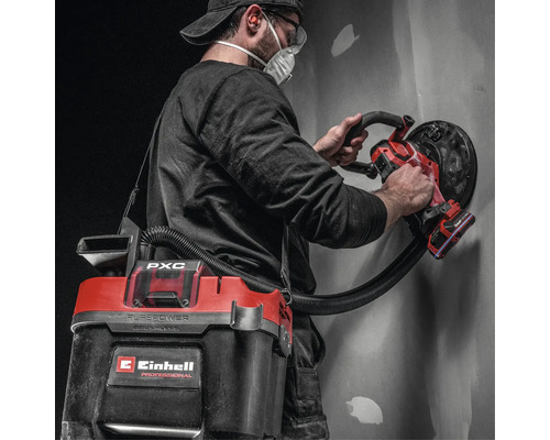 Artisan utilisant une ponceuse murale sans fil Einhell avec aspirateur sans fil raccordé pour poncer un mur.
