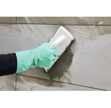 Main portant un gant de protection lors du jointoiement de carrelage avec une taloche