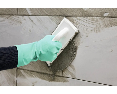 Main portant un gant de protection lors du jointoiement de carrelage avec une taloche
