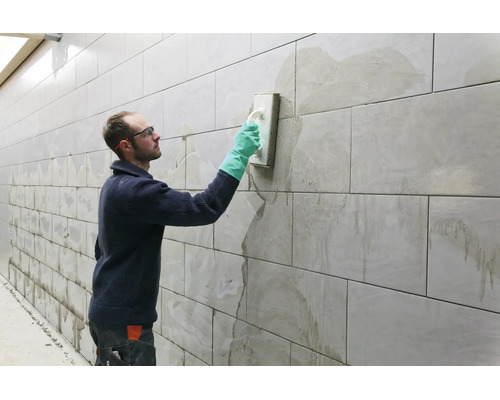 Artisan jointoyant un mur carrelé avec une taloche et des gants de protection