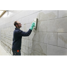 Artisan jointoyant un mur carrelé avec une taloche et des gants de protection